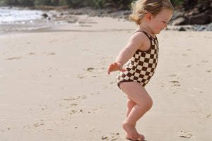 Child in a checkered swimsuit walking on a sandy beach.