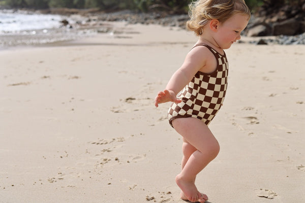 Child in a checkered swimsuit walking on a sandy beach.