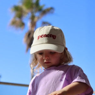 Child wearing a white cap with text saying 'peachy'