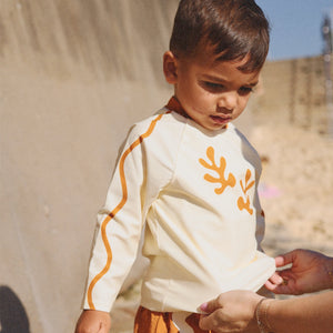 Child wearing a white long-sleeve rash vest with orange abstract print