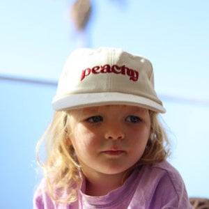 Child wearing a white cap with 'peachy' embroidered on it