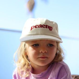Child wearing a white cap with 'peachy' embroidered on it